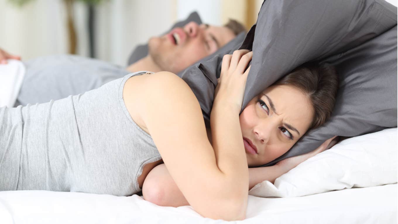 Woman Refuses To Share A Hotel Room With Her Husband's Teen Brothers uncomfortable woman holding pillow over ears in bed next to man snoring
