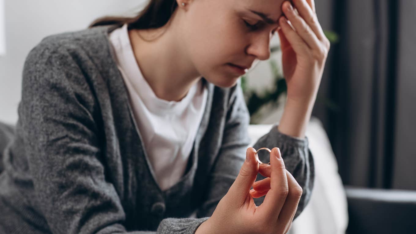 Man Refuses To Let His Fiancée Continue Living With Him After She Broke Off Their Engagement sad woman holding wedding ring sitting alone on sofa