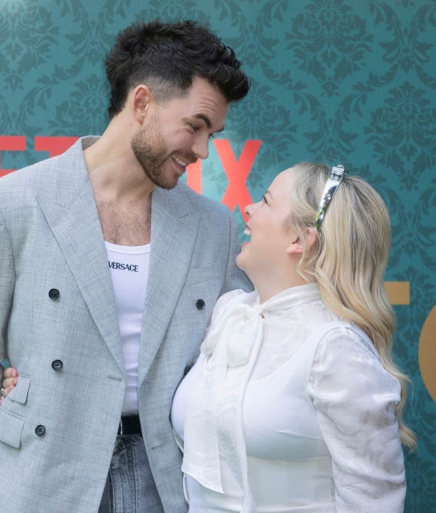 Nicola Coughlan and Luke Newton smiling at each other on the red carpet