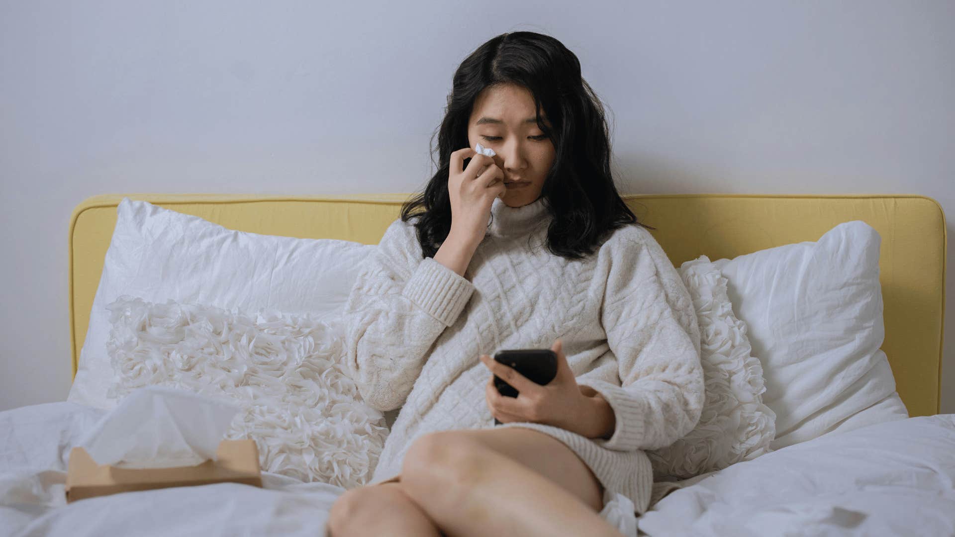 crying woman in bed on her phone