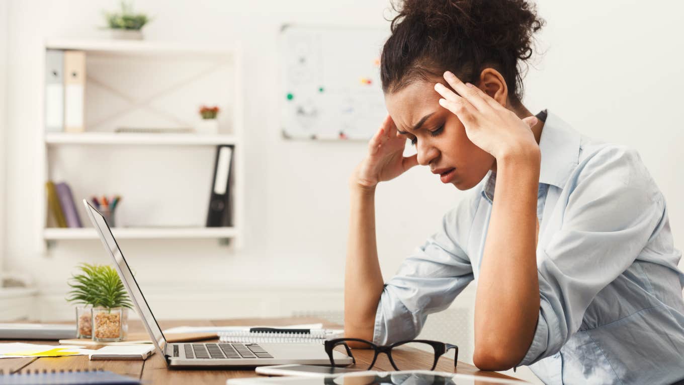Worker Admits She's Close To A Full Breakdown At Work Because She Didn't Use PTO Days To Rest tired woman with fingers on temple sitting at desk in front of computer