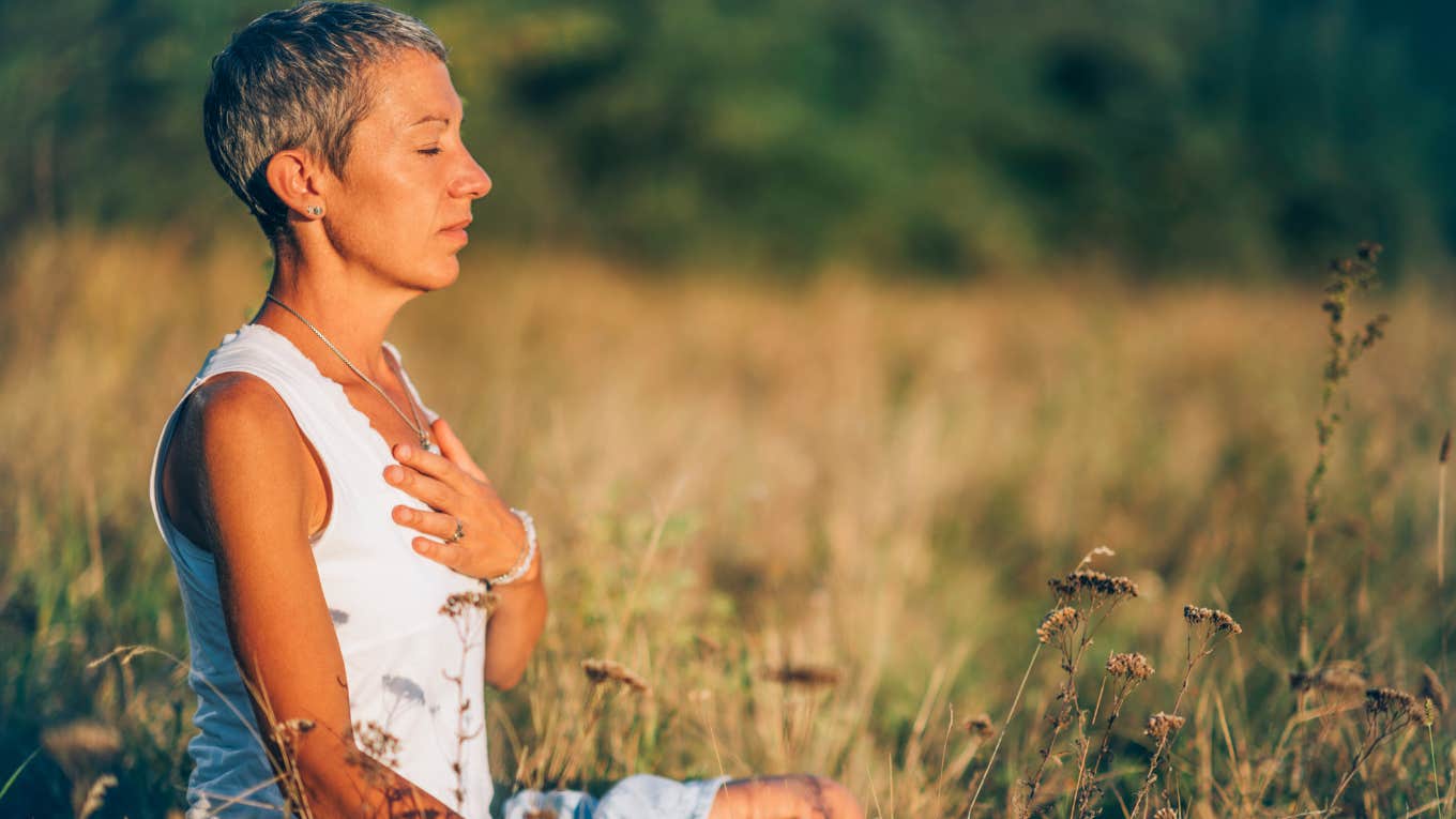 Manifestation Expert Reveals The 'Power Move' That Will Help You Worry Less woman meditating and manifesting in a field outside
