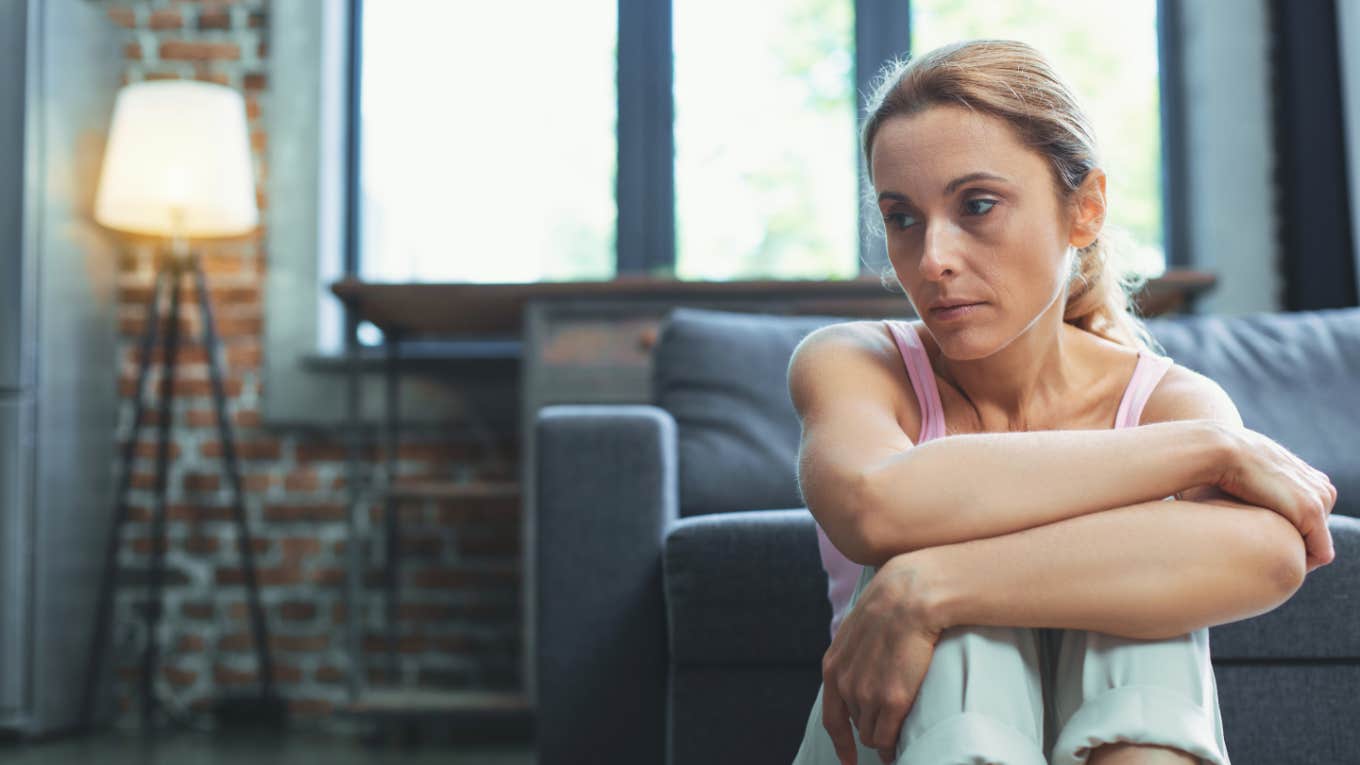 Newly Estranged Adult Child Admits They Live With Guilt & Fear Of Punishment grieving woman arms crossed over legs at home