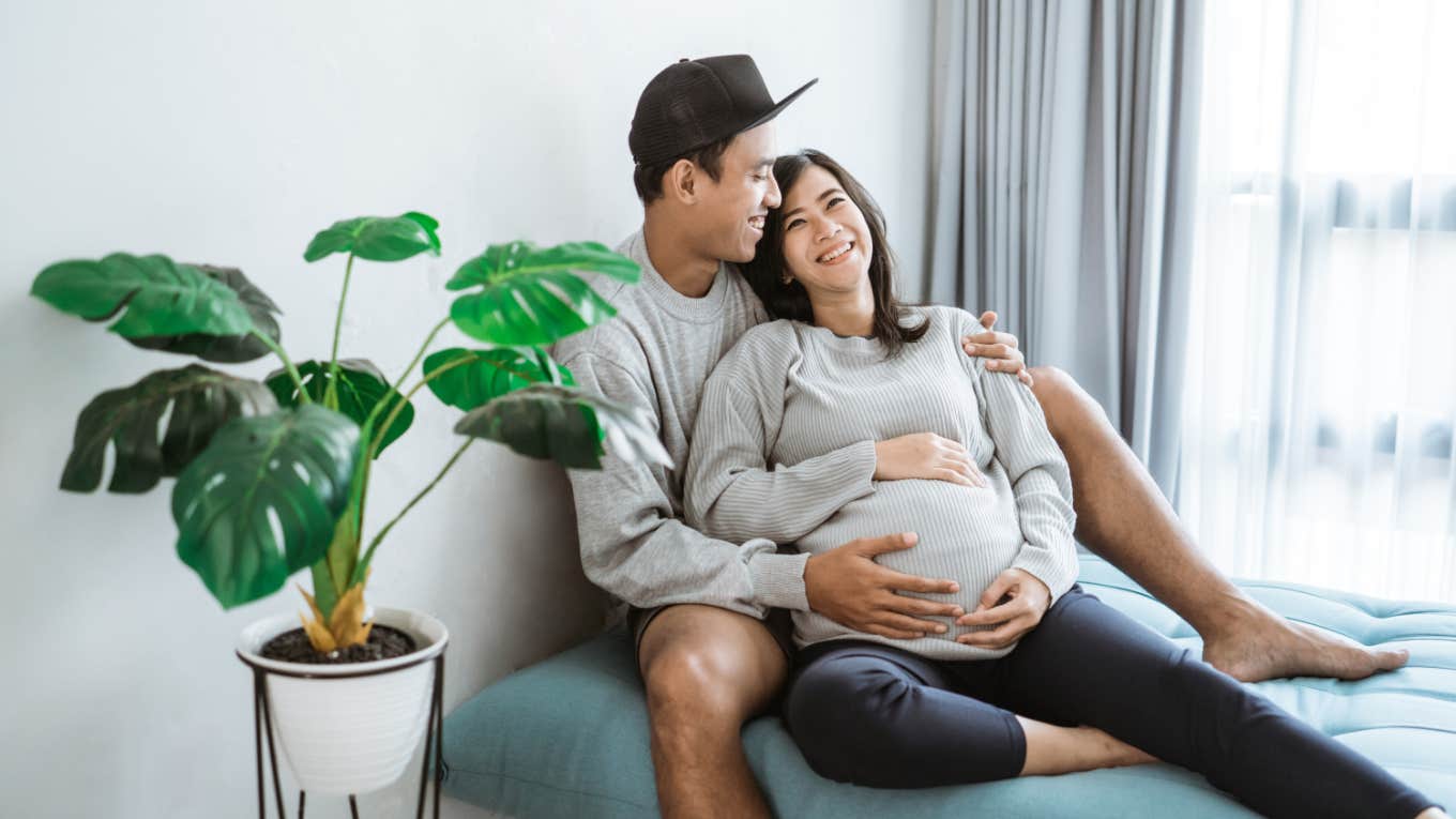 Pregnant Woman Tapes Melons To Her Boyfriend’s Body So He Can Feel What It's Like to Be Pregnant man and pregnant woman embrace each other while sitting by window at home