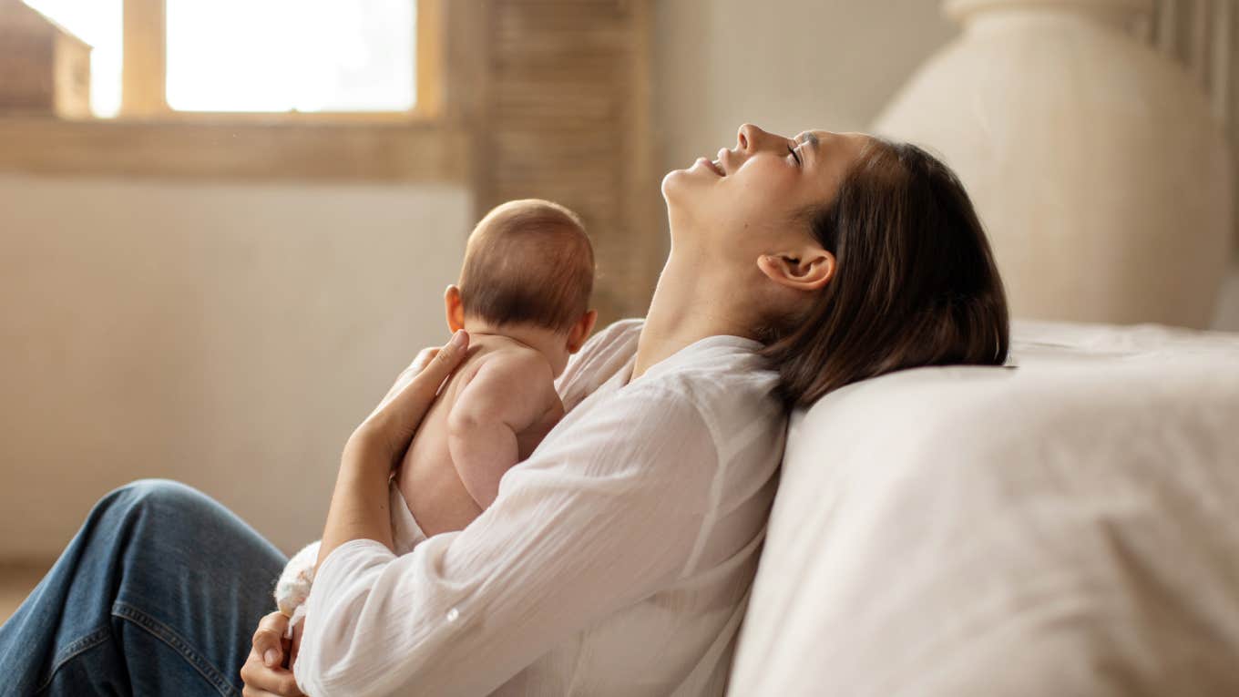 Mom Says She Finds Parenting To Be A Deeply Unsatisfying Role Tired young mother sitting on floor and holding newborn baby on hands