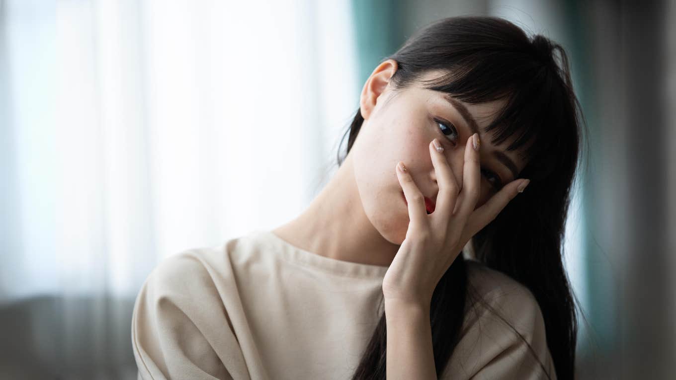 5 Personality Traits That Suggest You Were Raised In A Predominately Negative Home, According To Family Therapists Woman with her hand on her face, negative home life