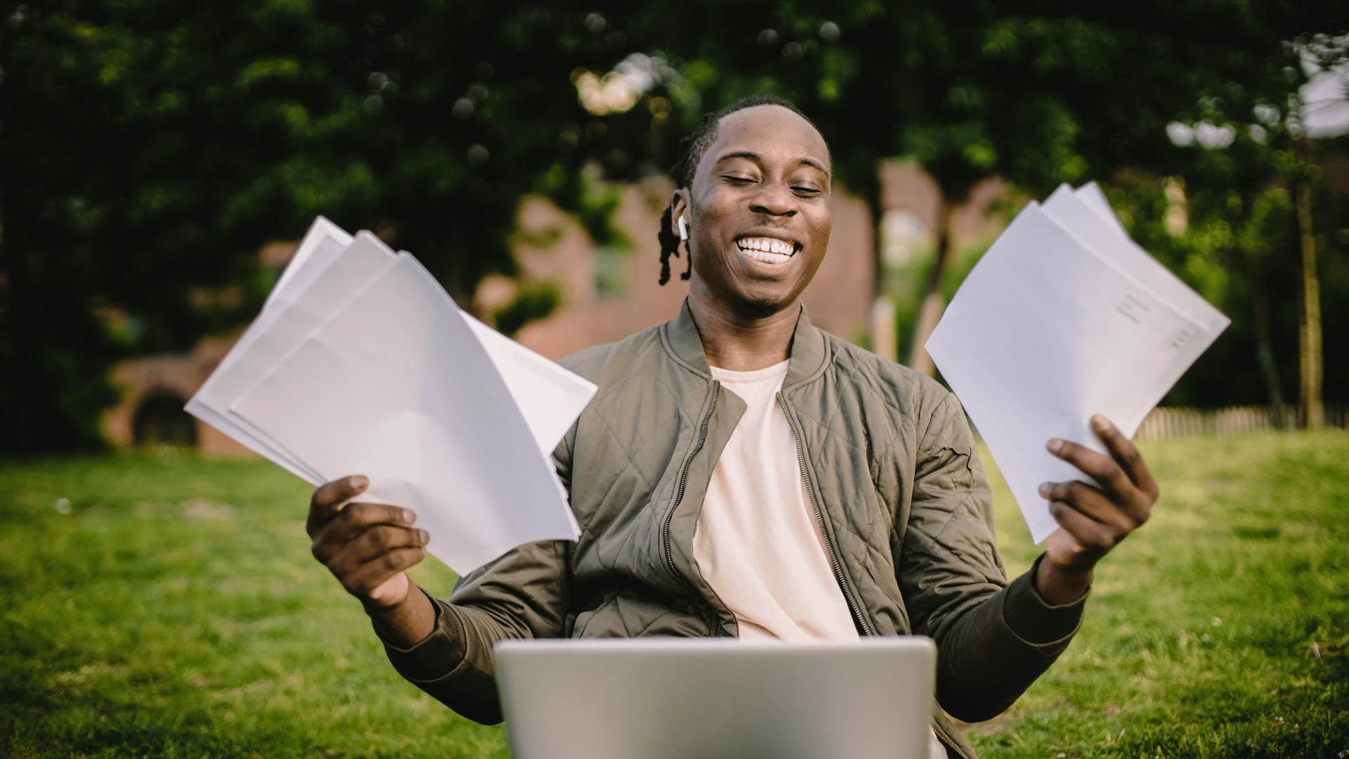 smiling man with open laptop and holding papers