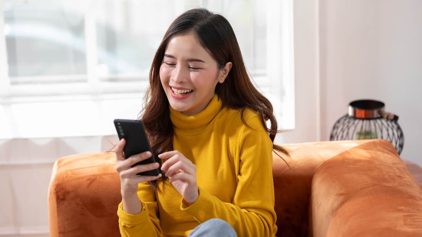 Almost Half Of Gen Z Wish Social Media Didn’t Exist young woman smiling at phone sitting on couch