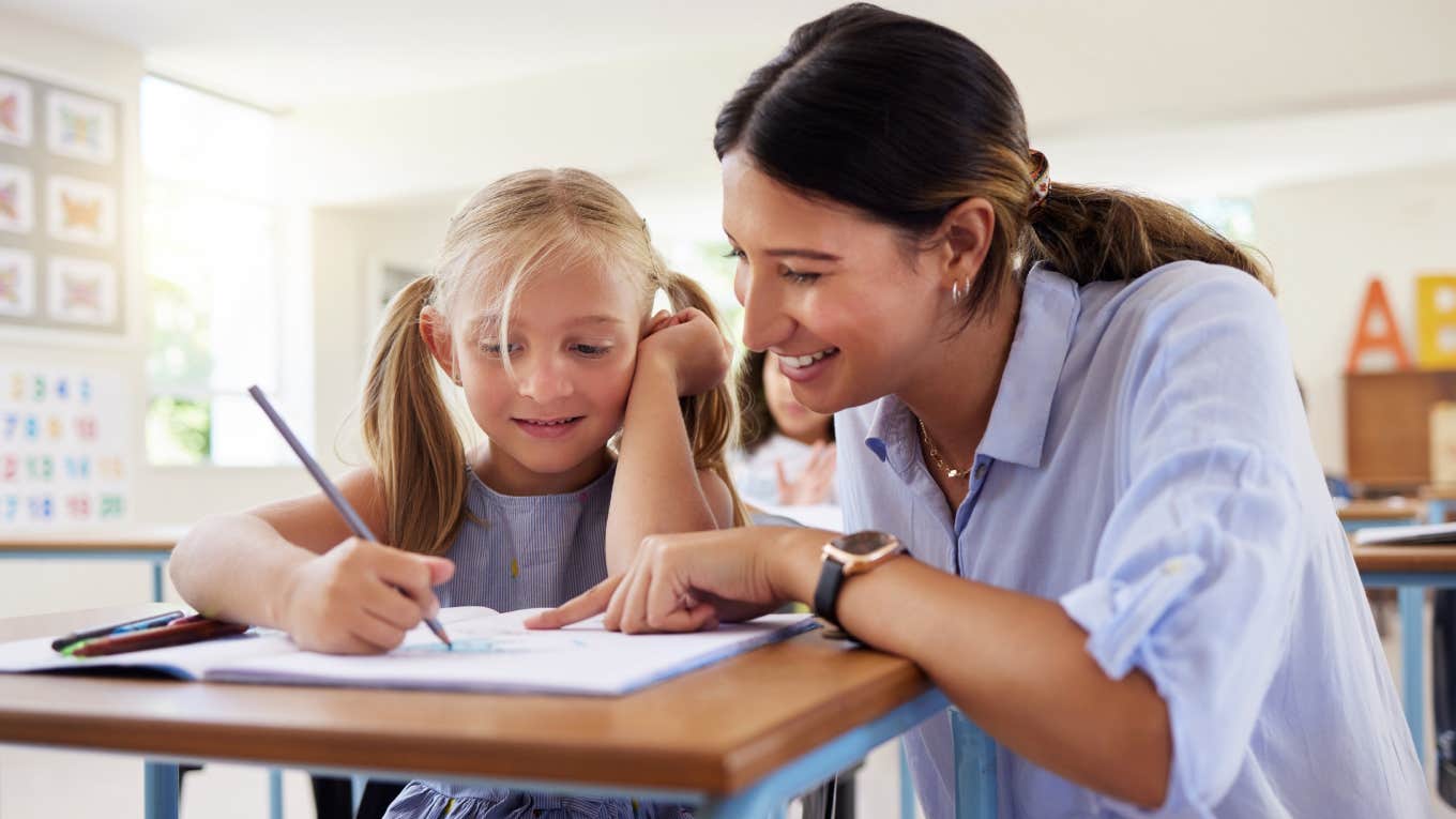 Teacher Says She's Sick Of Our Education System Being Used As A Band-Aid For Society's Problems teacher helping little girl with assignment in classroom