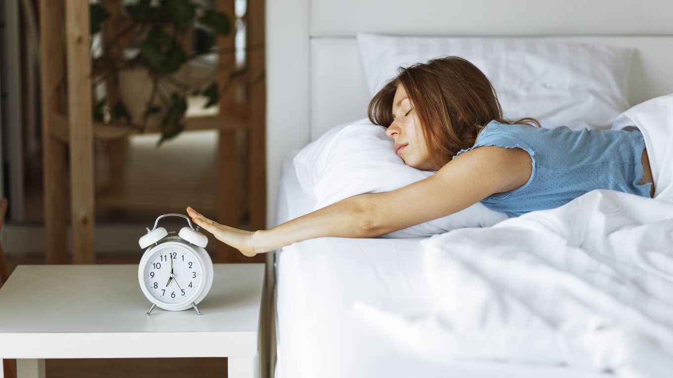 Wellness Expert Reveals Why You Shouldn’t Set Multiple Alarms In The Morning Woman snoozing her alarm in the morning