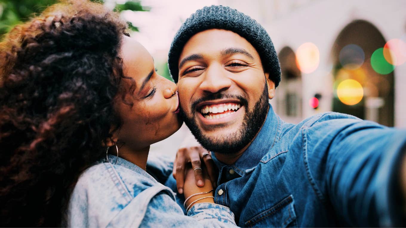 Crucial Things You Must Fully Accept About Your Partner Woman clinging to mans side, embracing a big kiss on the cheek.