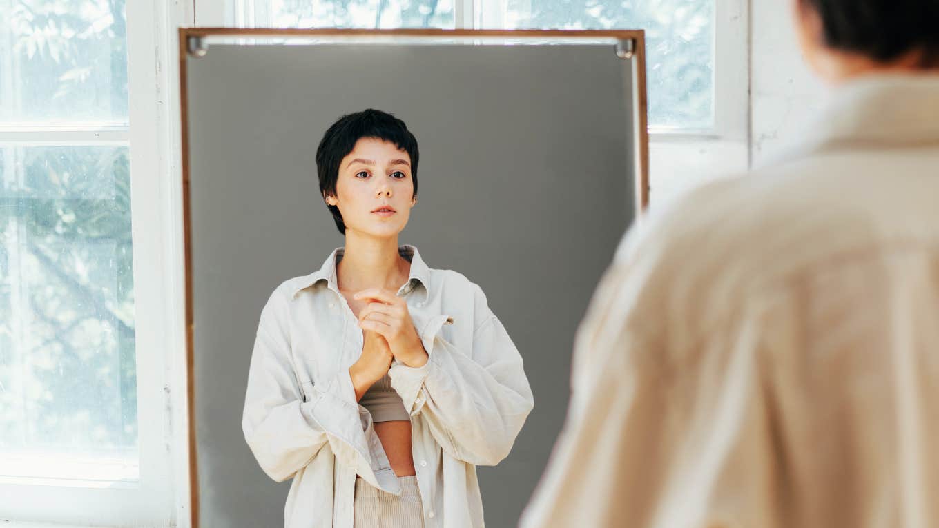 Expert-Approved Ways To Feel Better About The Way You Look Woman looking at herself in mirror.