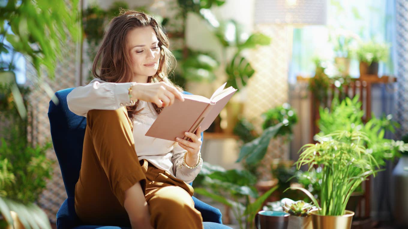 Report Details How Many Day People With Unlimited PTO Actually Take Off Each Year relaxed trendy middle aged woman with long wavy hair with book in green pants and grey blouse in the modern living room in sunny day.