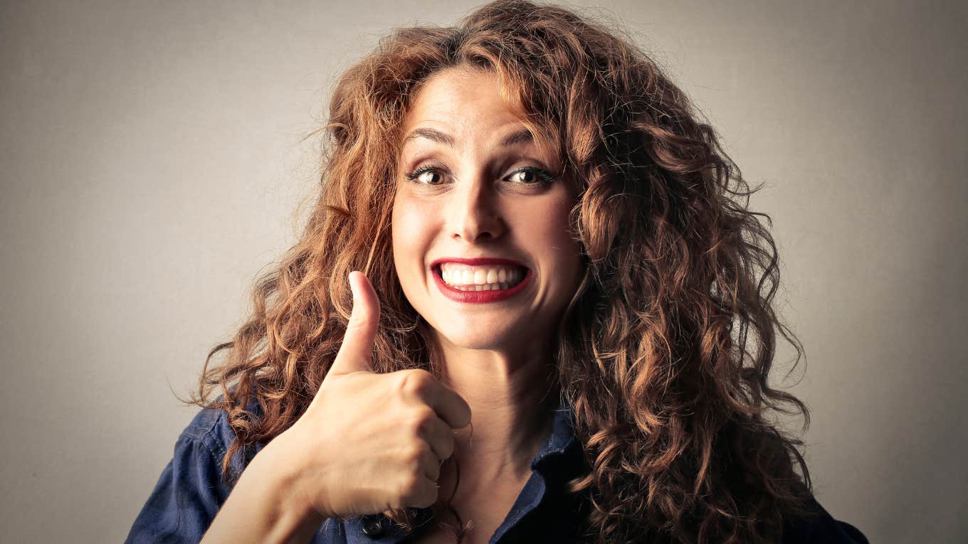 Psychologist Shares 2 Ways Parents Subconsciously Teach Their Kids To Become People-Pleasers Woman with curly red hair giving an enthusiastic thumbs up