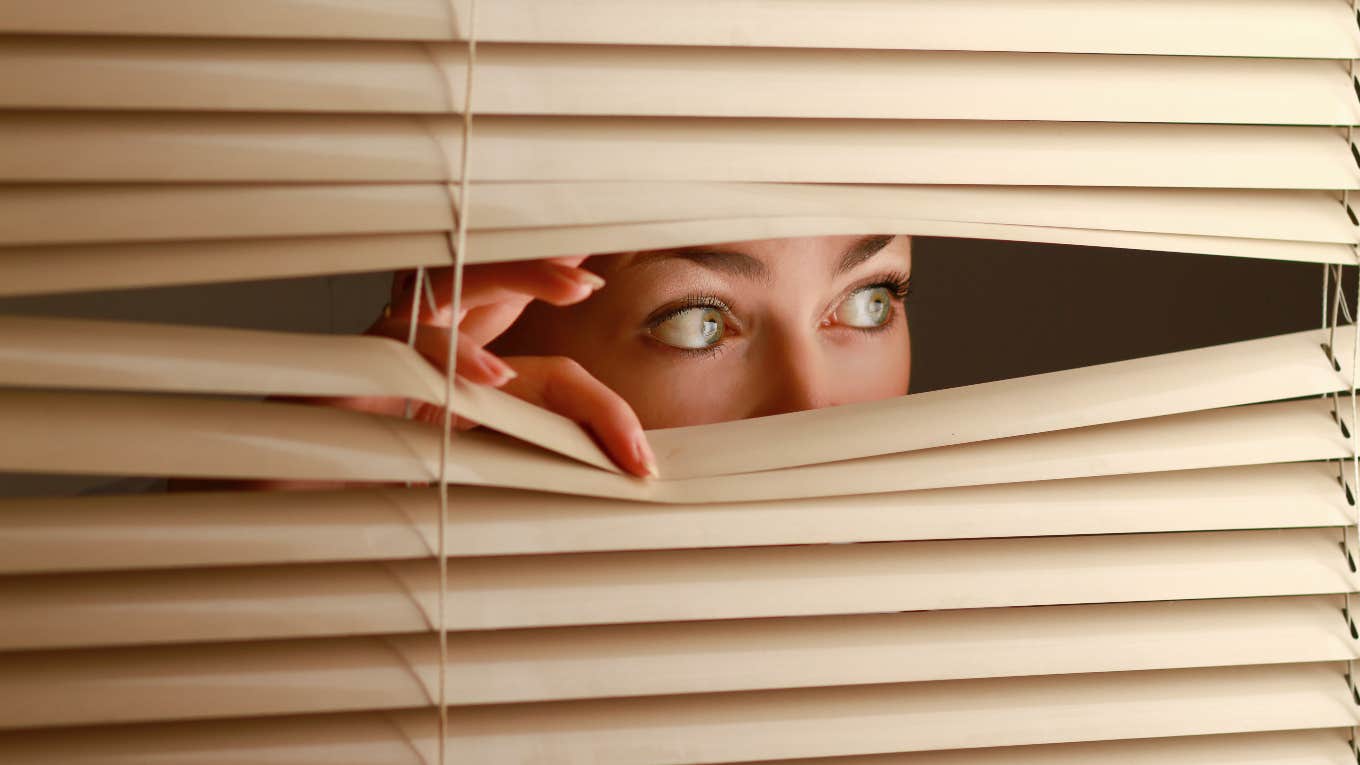 Woman Thought Her House Was Haunted After Finding Rug Buried In Her Yard woman looking out the blinds of haunted house at rug buried in backyard