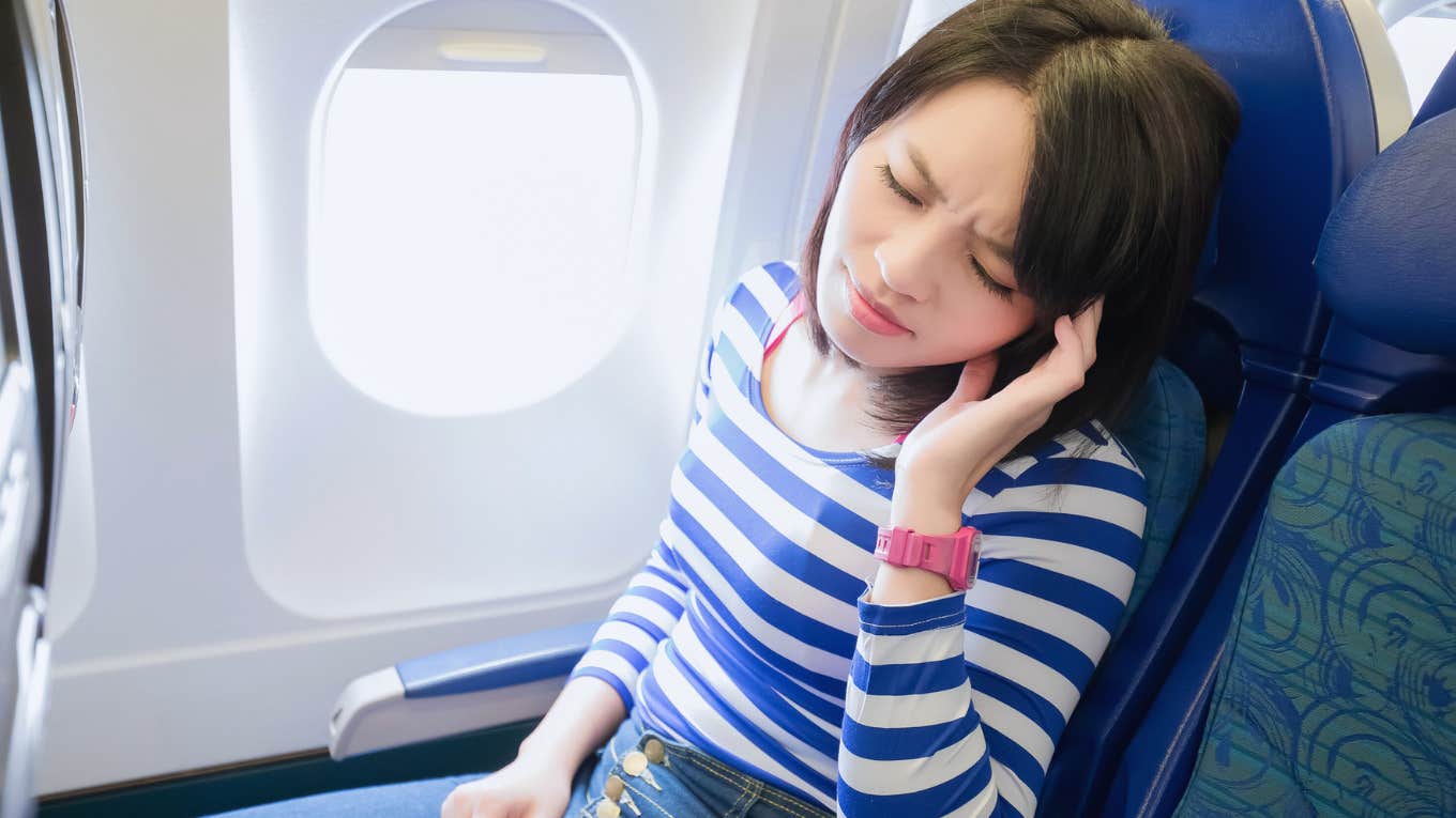 Woman’s Rich Boyfriend Wants To Fly First Class While She Sits In Economy Woman sitting in economy airplane seat looking annoyed.