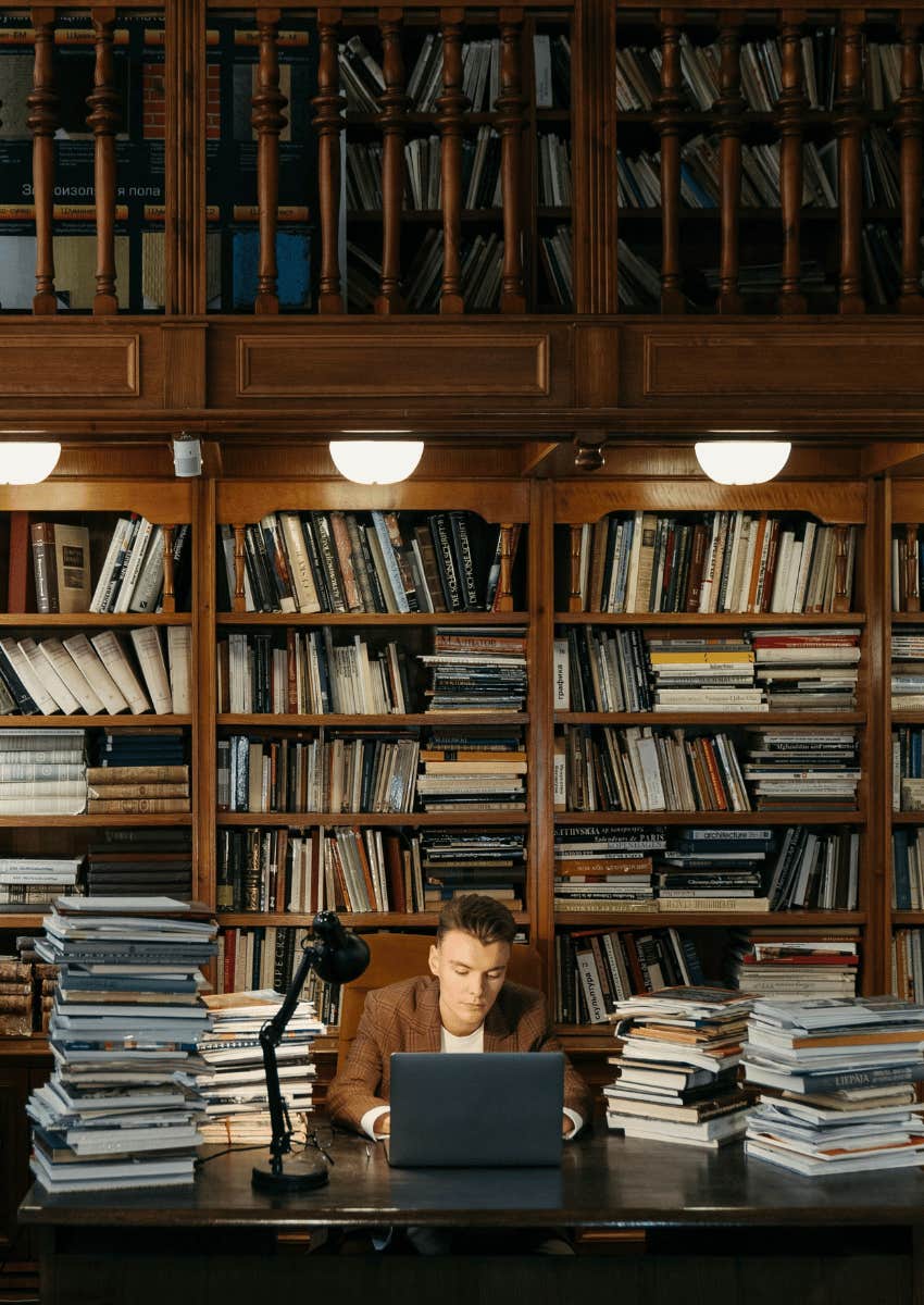 young man on a laptop surrounded by books