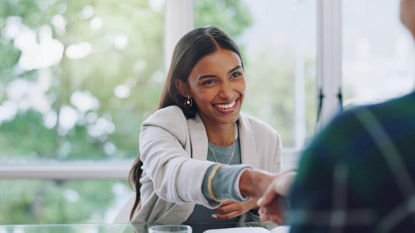 Career Coach Reveals Attribute Sought After By Every Hiring Manager smiling business woman reaching out for a handshake in an interview