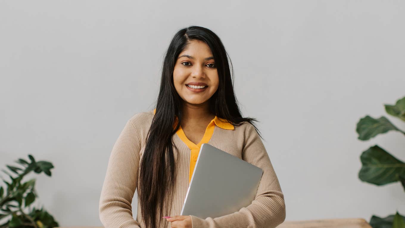 Job Search Expert Shares The One Piece Of Information To Delete From Your Resume professional woman smiling while holding laptop
