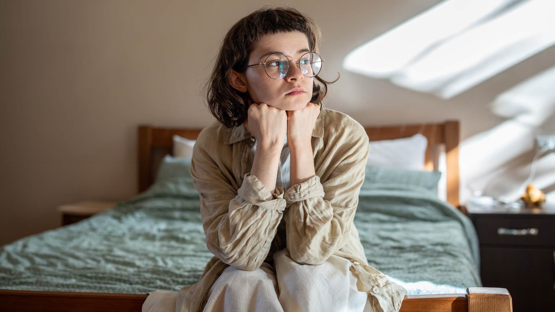 Woman sitting on her bed looking sad.