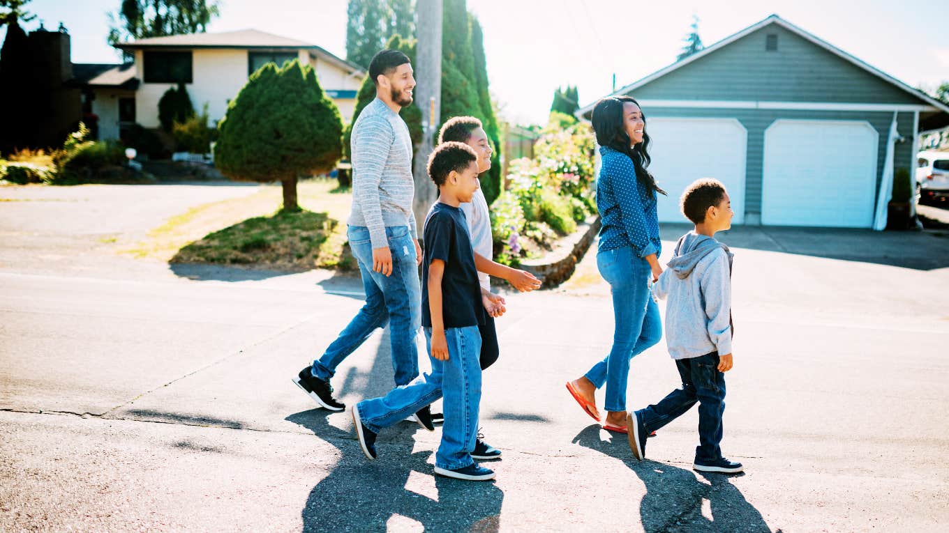 The Suburbs Are Making A Comeback — Have We Learned Nothing? Family walking in front of homes in suburbs.
