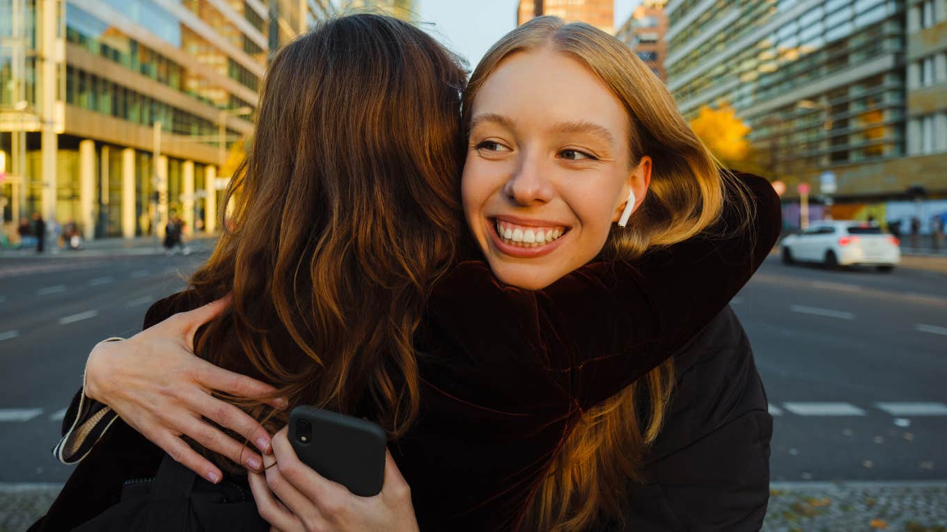 Things Millennials Are Tired Of At This Stage In Their Lives Smiling young woman in earphones hugging her friend when they meet at city street