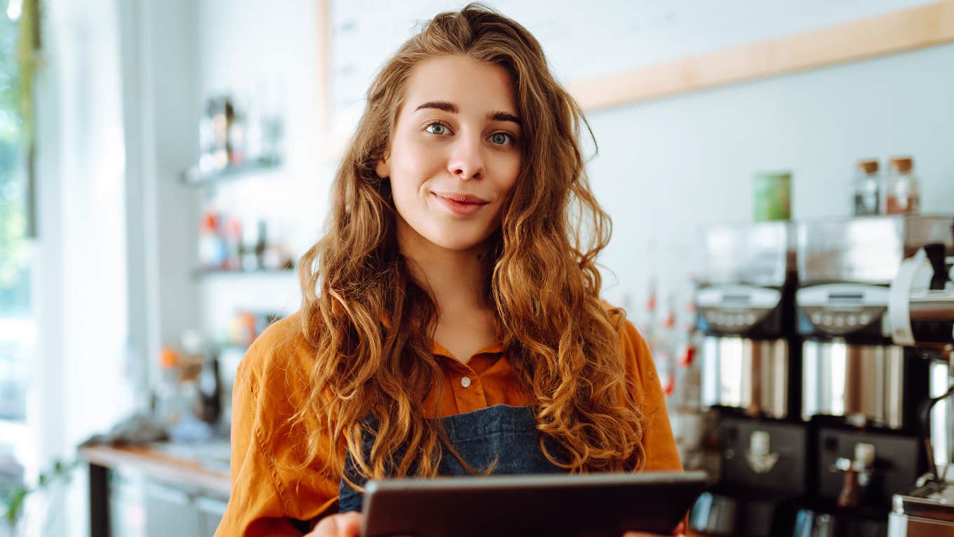 Brilliant Habits Of High Achievers Who Work Less Than The Rest Of Us Beautiful woman owner stands behind the counter of a coffee shop.