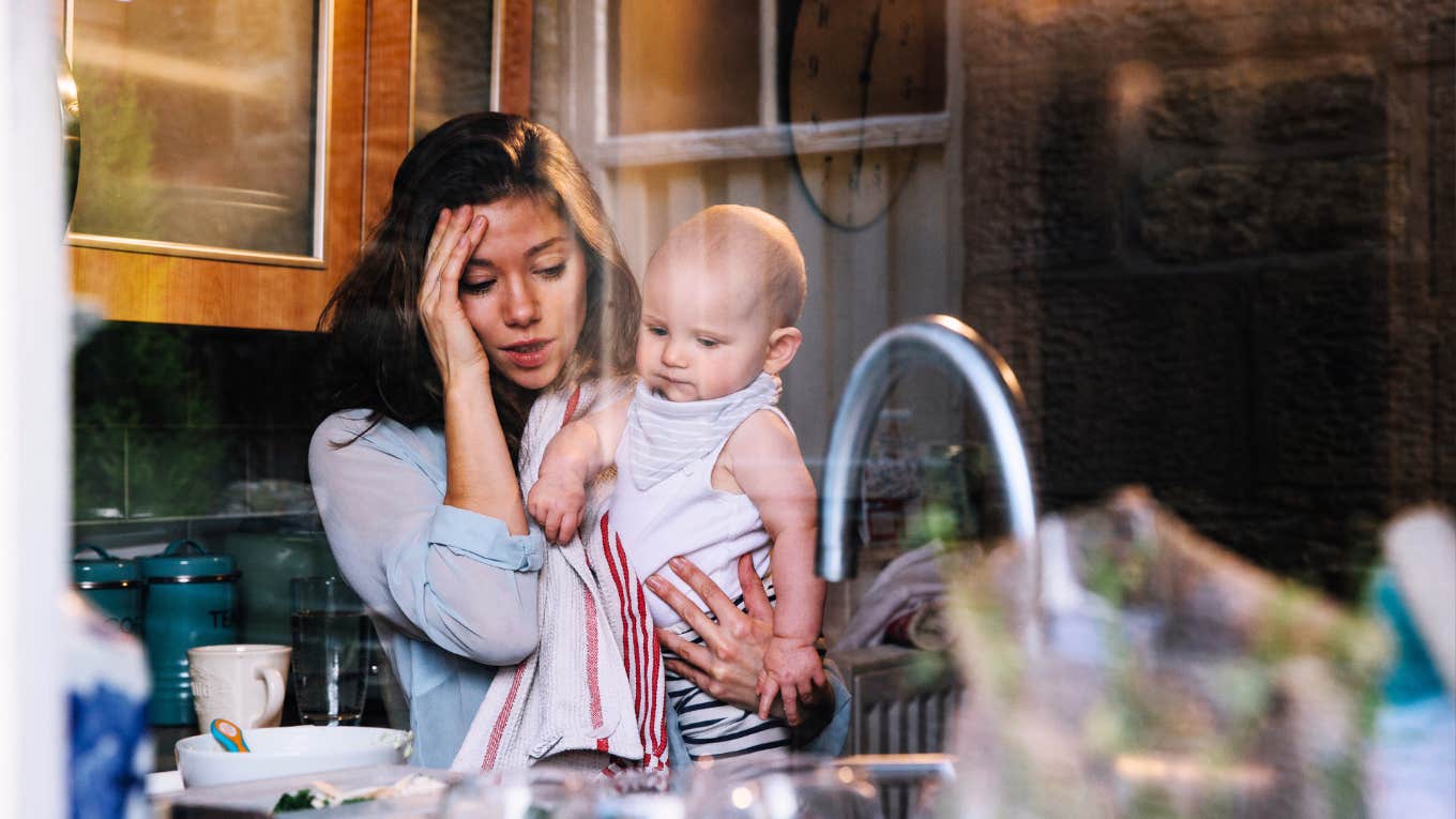 Wife stressed out standing in kitchen with baby.
