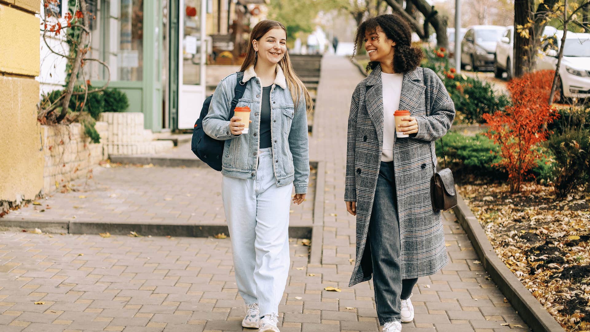 two women walking and talking while drinking coffee