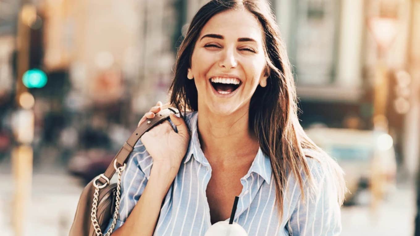 Playful Traits Of Women Who Always Attract Attention, According To Psychology Playful woman smiling and laughing in street.