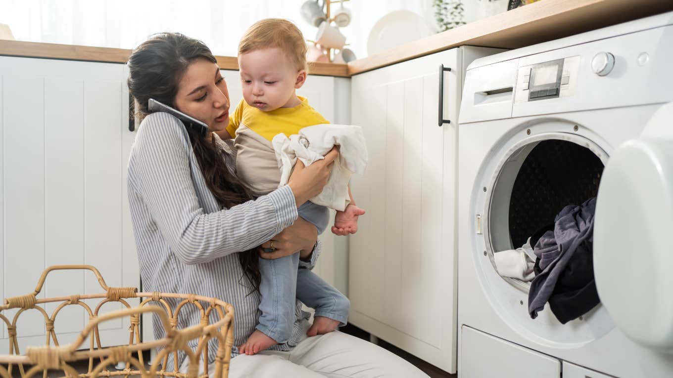 Recently Laid Off Mom Wants The 'Invisible Labor' She Does At Home To Be Acknowledged mom trying to do laundry while talking on the phone and holding toddler