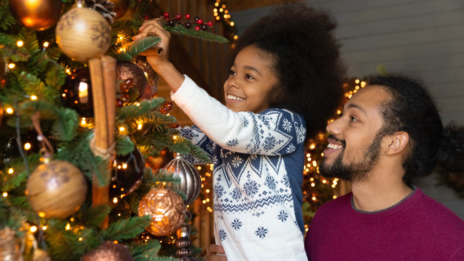 Young dad helping his daughter hang ornaments on the tree.