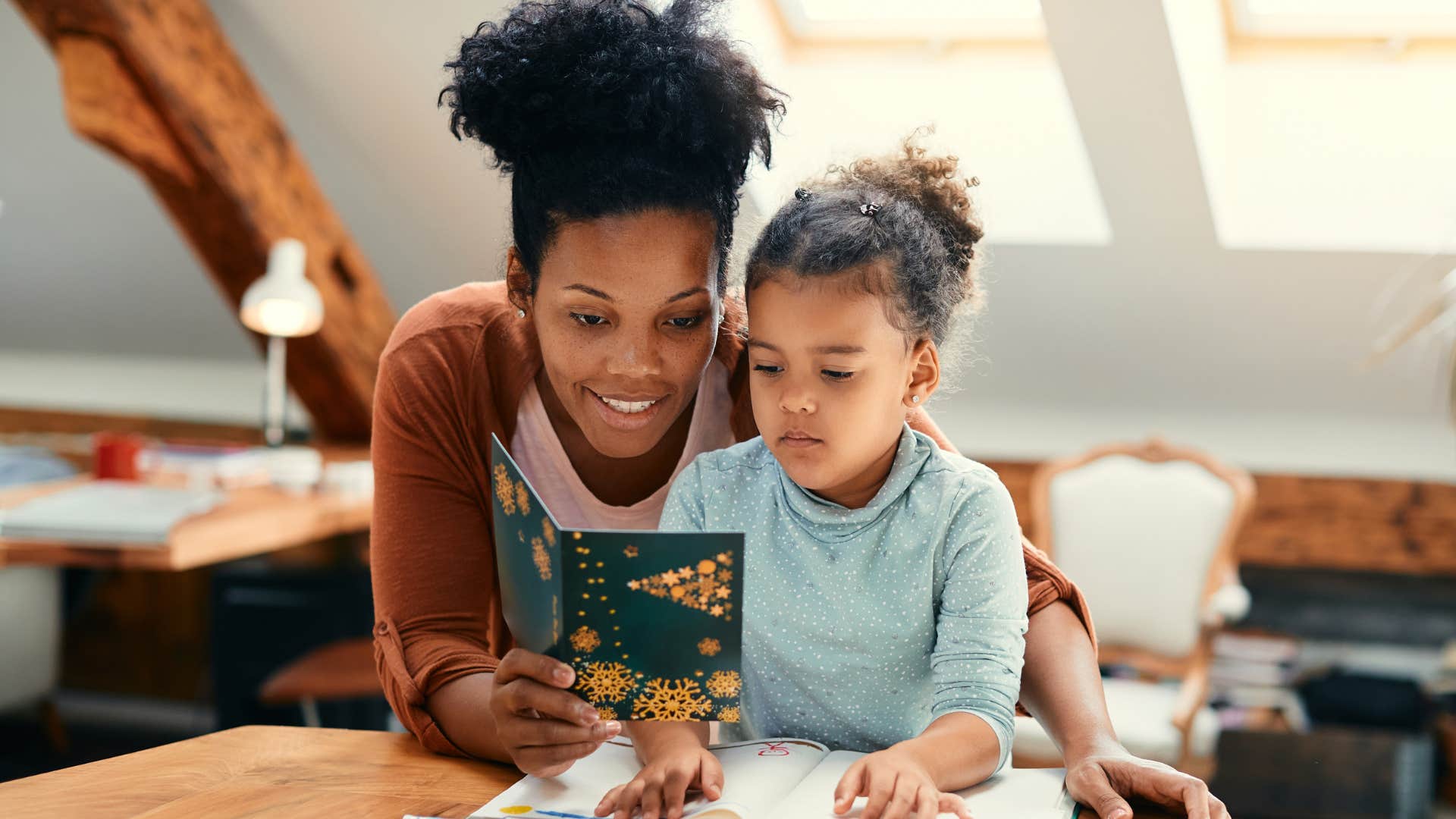 Woman smiling with her young daughter holding up a Christmas card.