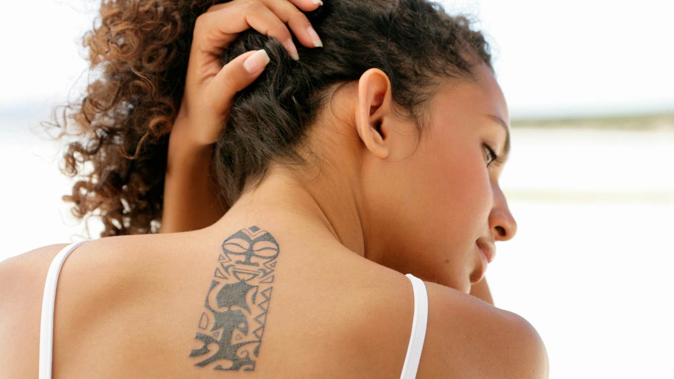 What Your Tattoo Placement Reveals About Your Personality, According To Psychology Woman holding hair up, showing back tattoo.