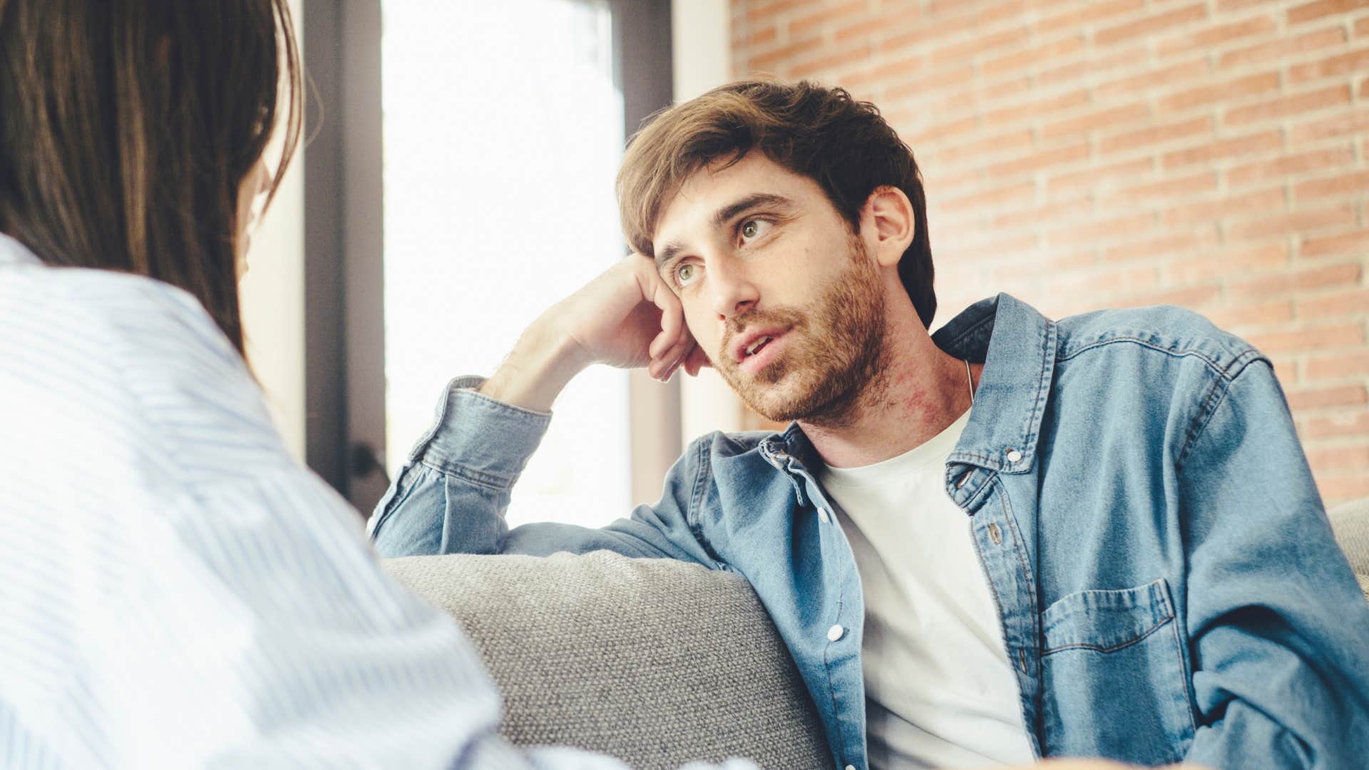 man seeking forgiveness sitting on couch talking to woman