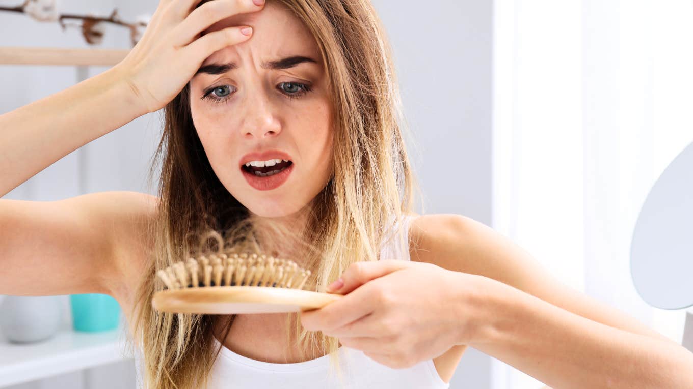 Why Is My Hair Falling Out? Research Says There's Unexpected Reasons Woman looking at hair brush, hair falling out.