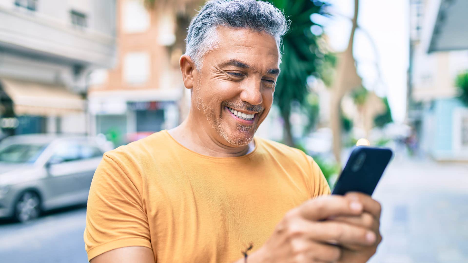 Older man smiling and texting on his phone