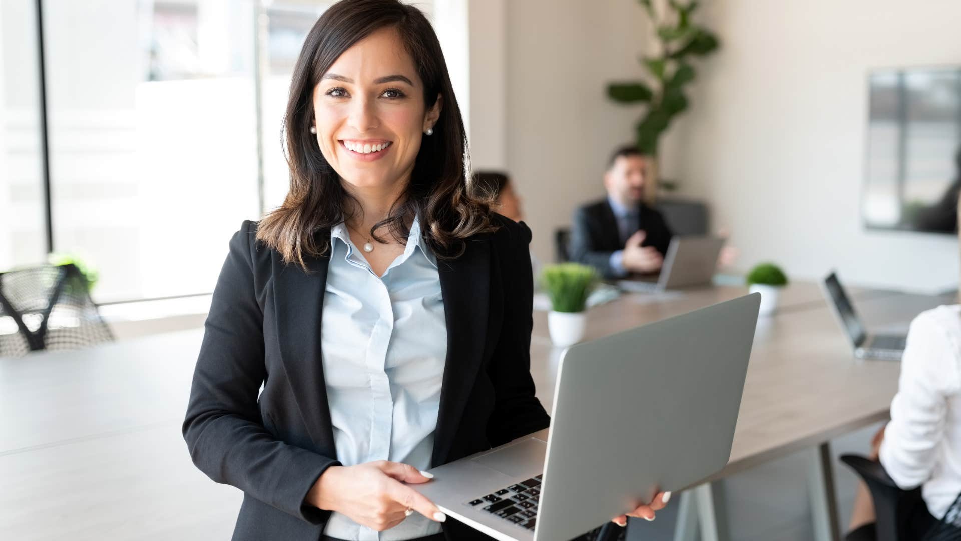 Woman smiling and holding her laptop in an office