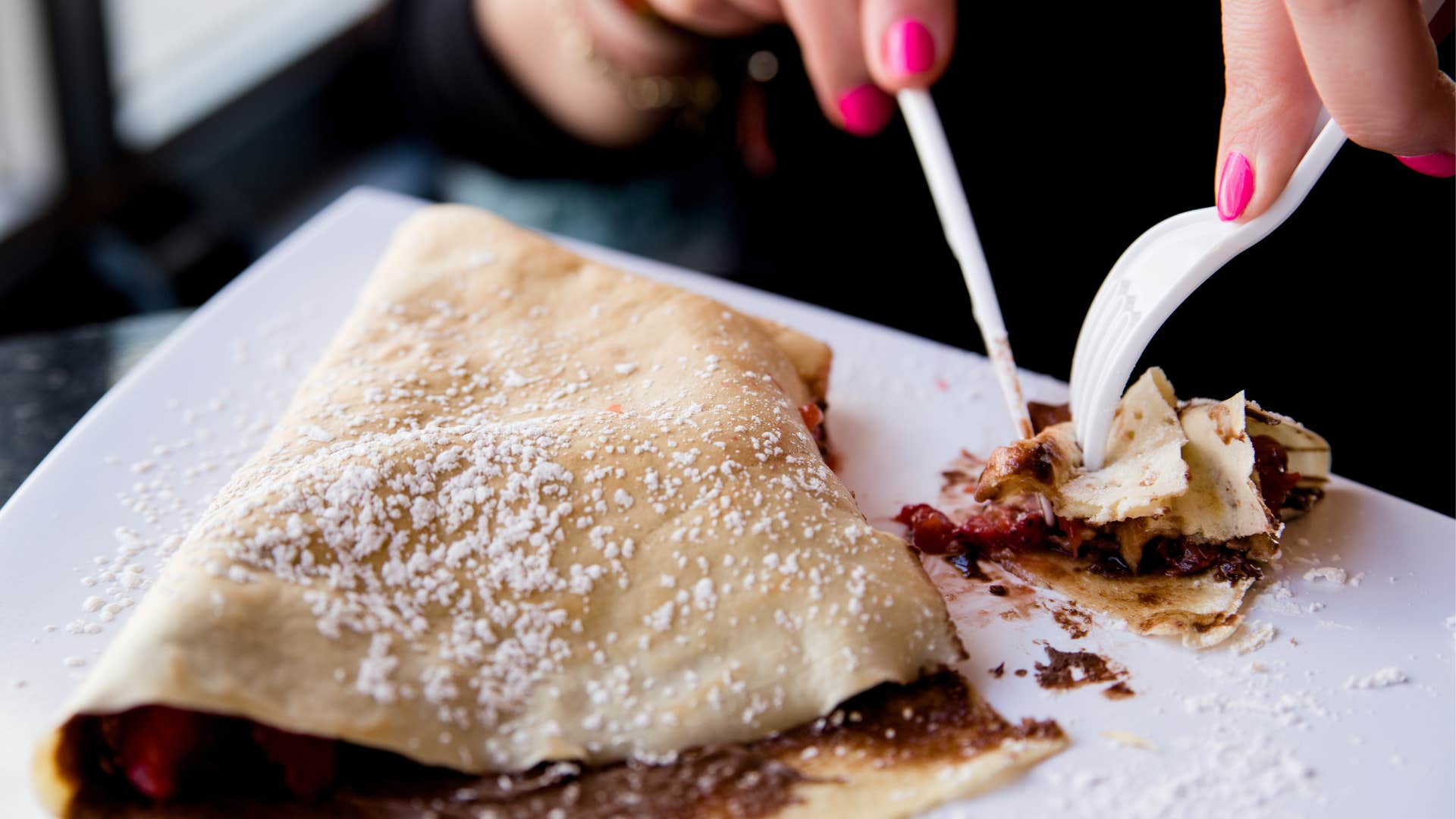 person using plastic utensils to eat a crepe