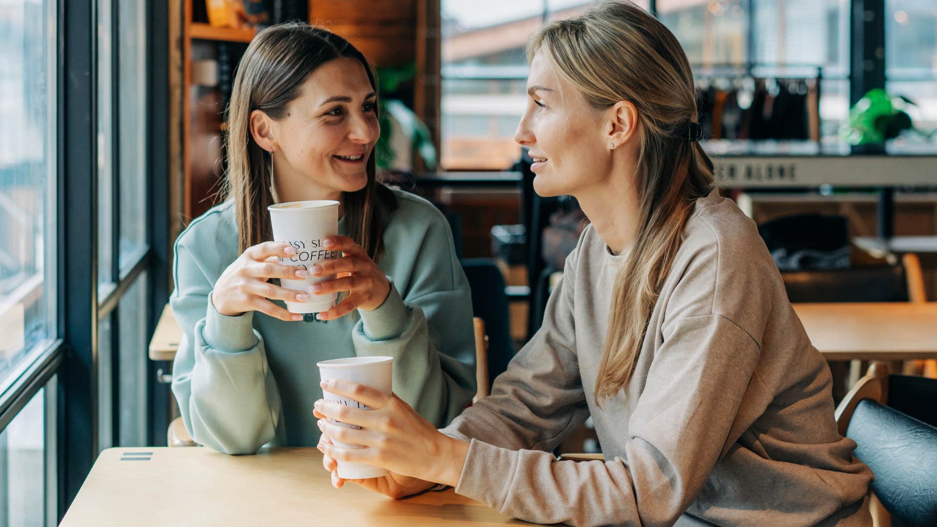 Two women smiling and saying she could care less in a coffee shop