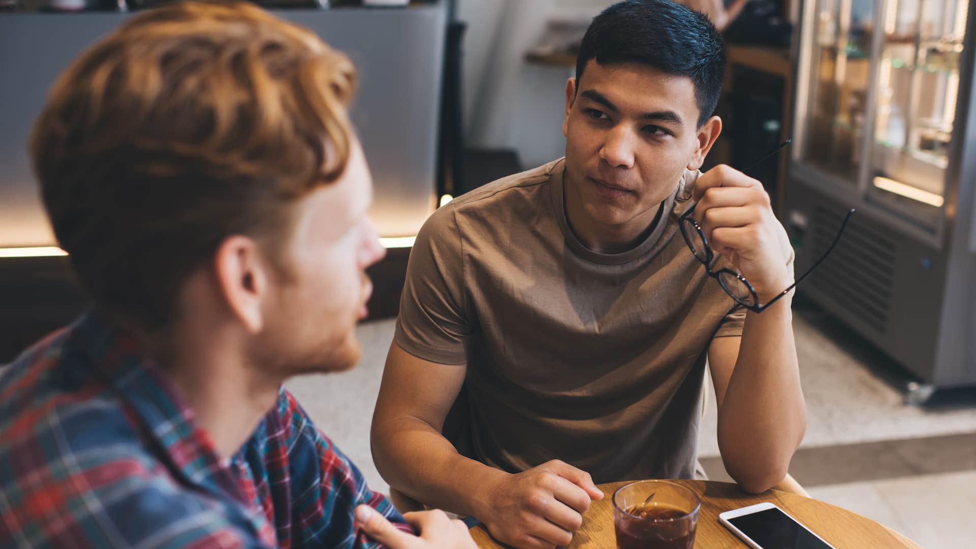Upset man listening to his friend explain there's no reason to talk like that in a coffee shop