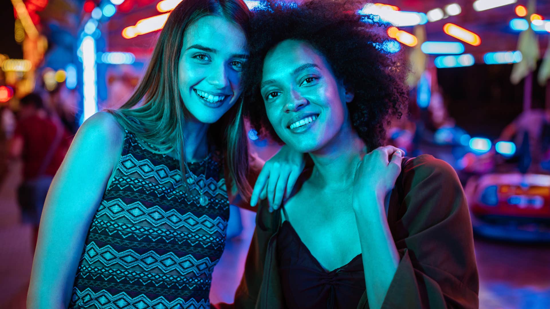 Two women smiling and hugging at a concert after buying affordable concert tickets