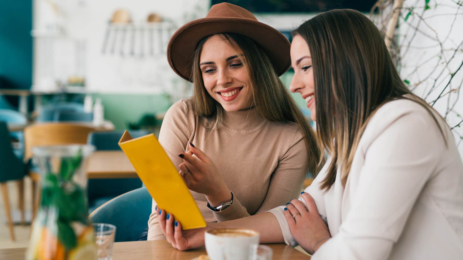 Two women smiling and looking at handheld menus at a restaurant