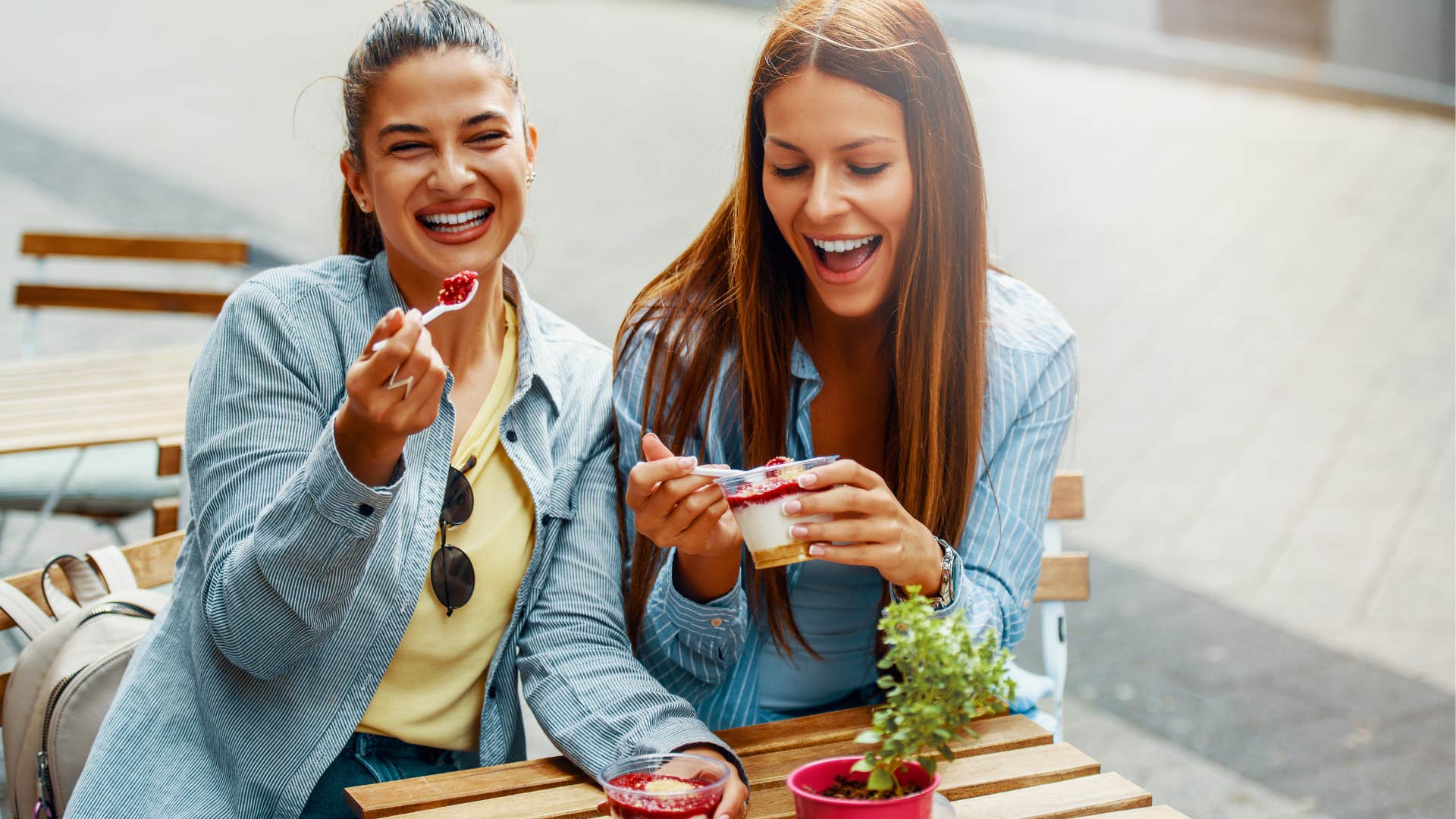 Two women smiling and consuming sugar ice cream outside at a table