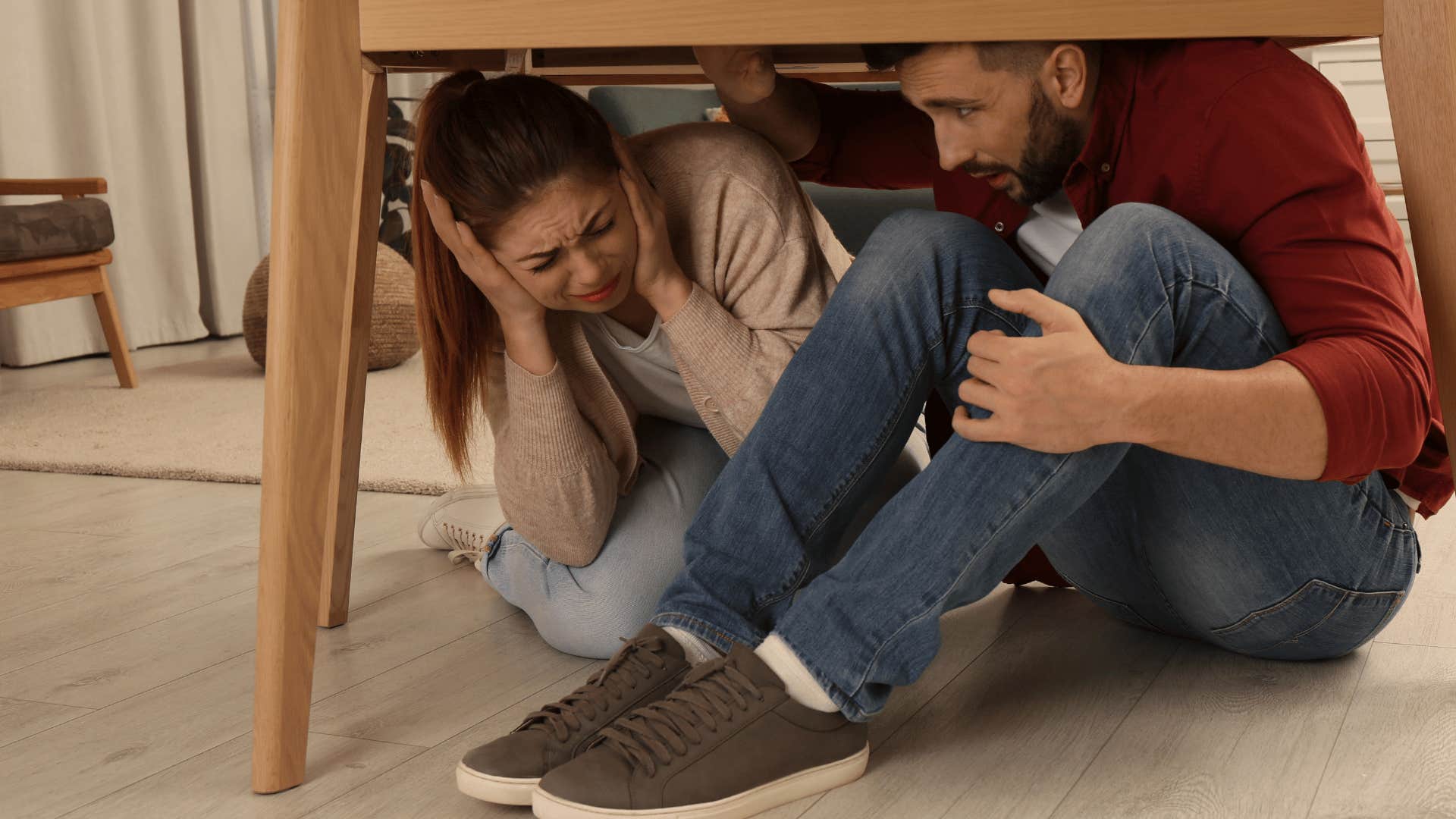 scared man and woman hiding under a table