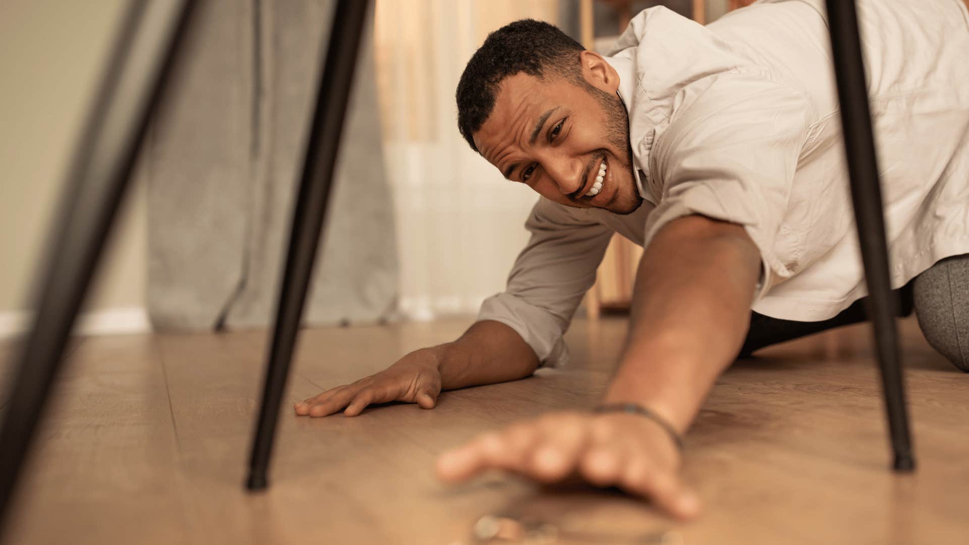panicked man reaching for keys under a chair
