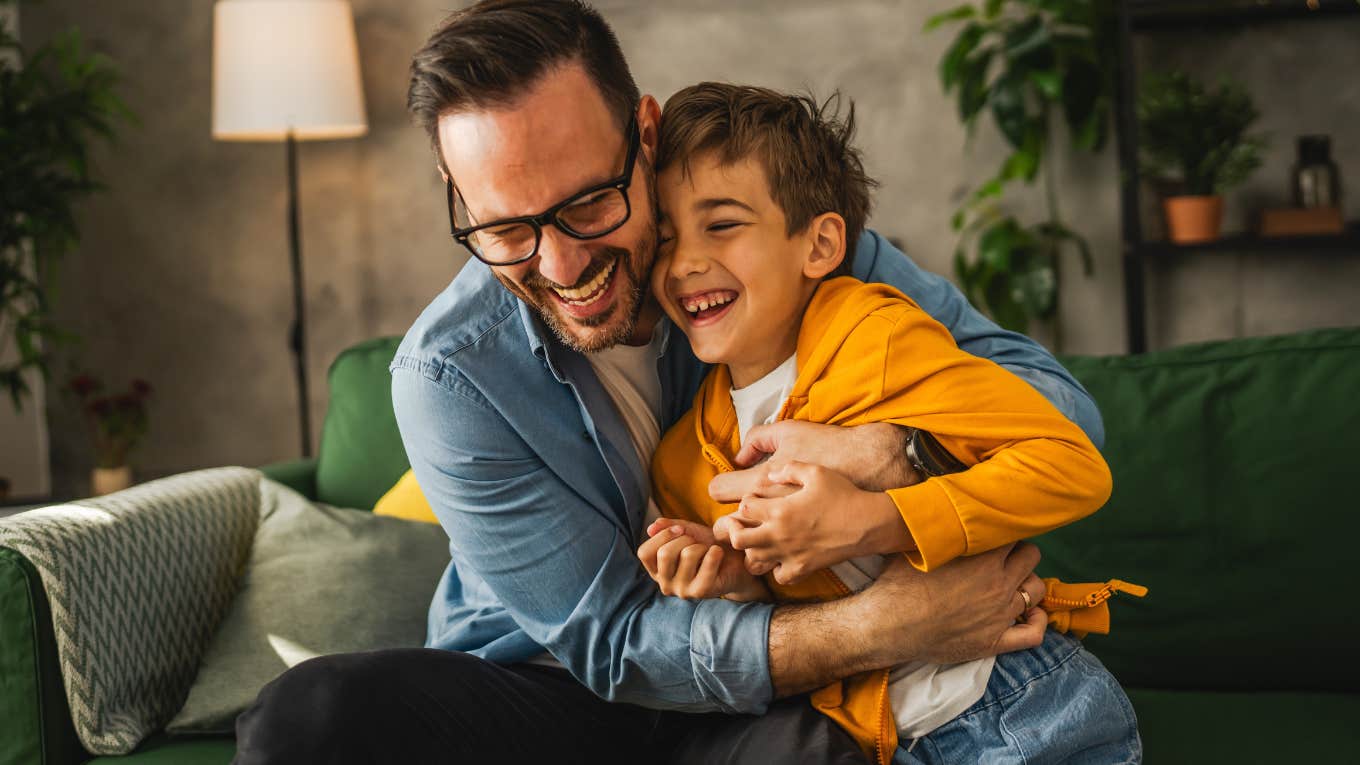 Man smiling and hugging his young son on a couch.