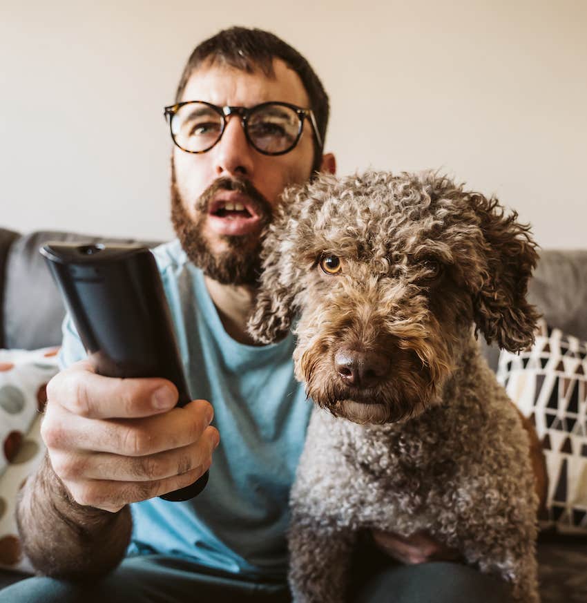 Man with remote control watches TV with his dog