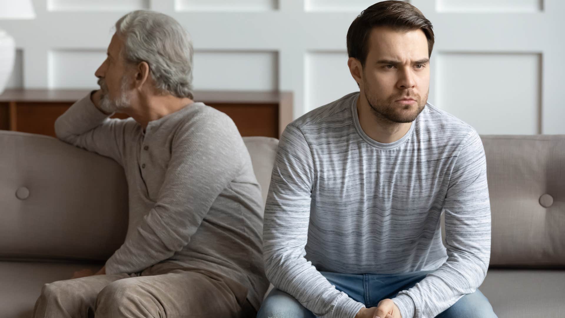 Upset dad turned away from his adult son on the couch