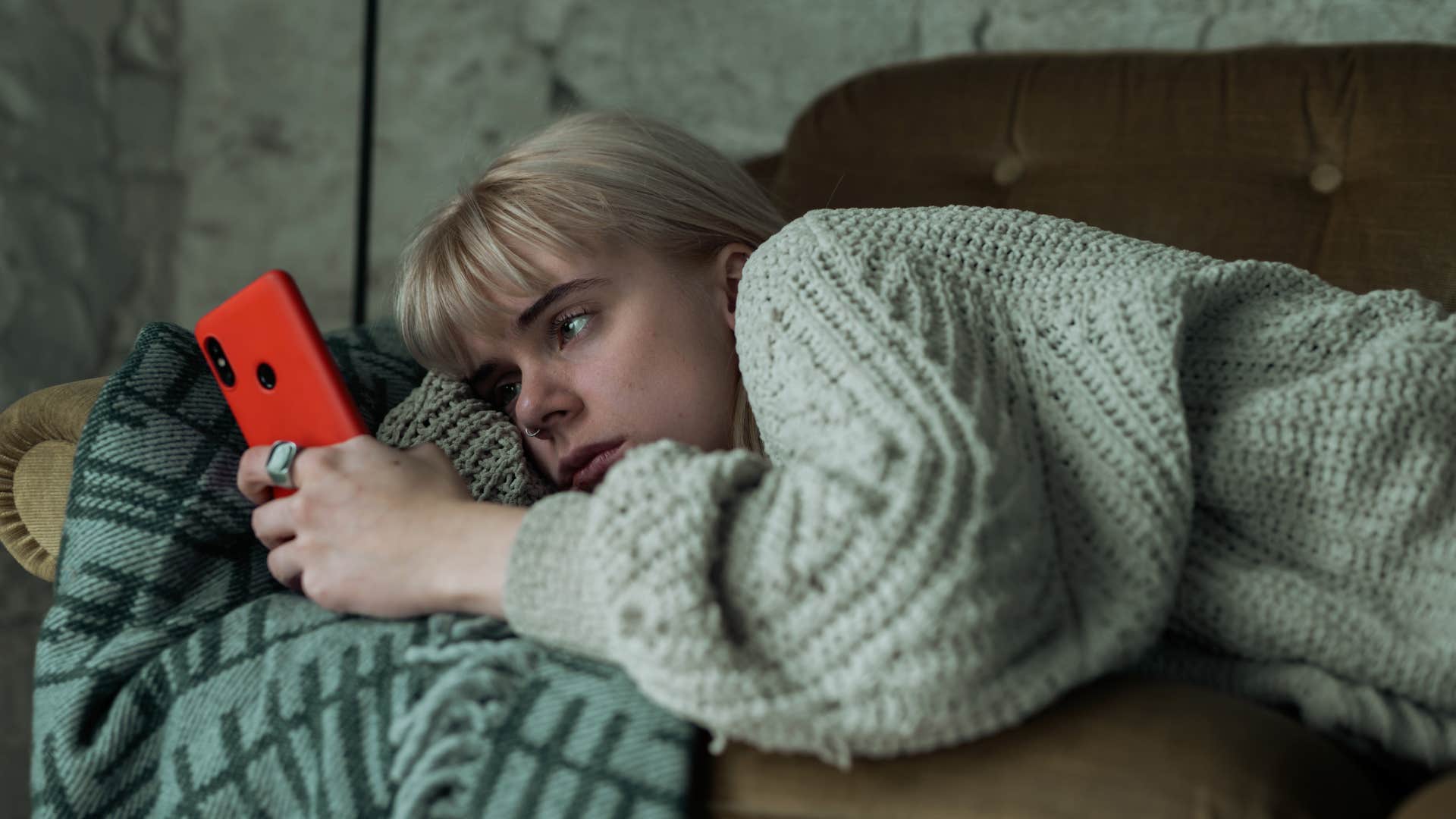 Upset Gen Z woman laying on a couch and looking at her phone.